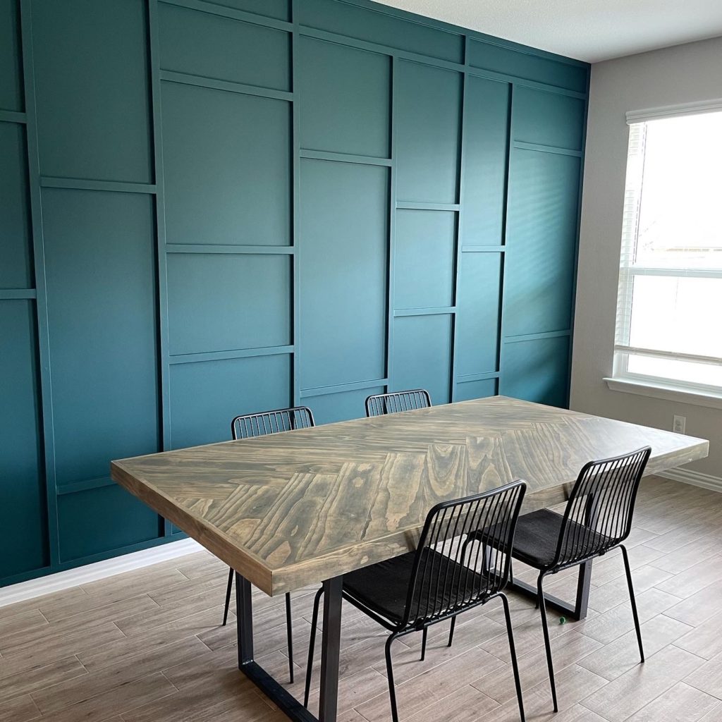 Picture of a Moody blue/green board and batten wall with a midcentury table and chairs in front. 